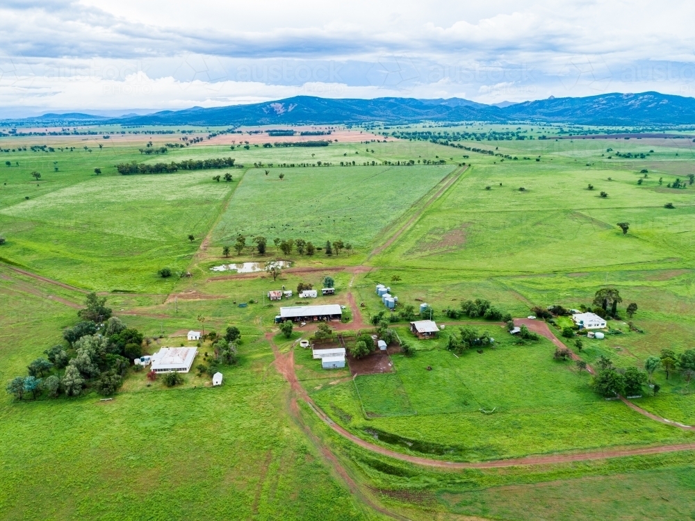 View of distant farm home area with house and sheds among green paddocks - Australian Stock Image