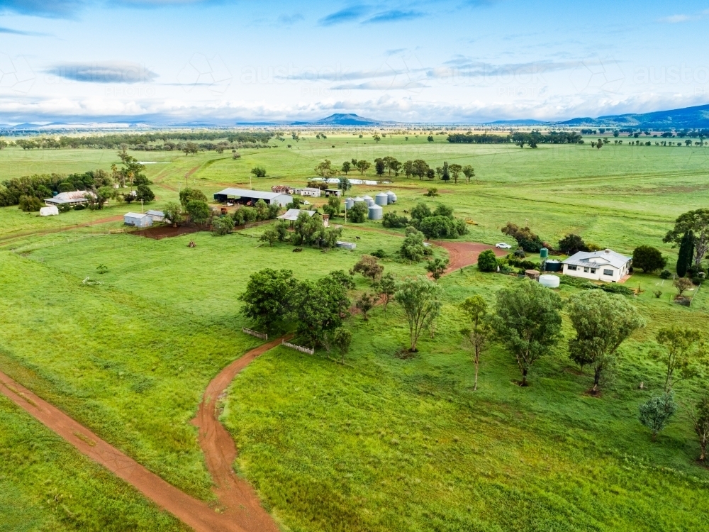 View of distant farm home area with house and sheds among green paddocks - Australian Stock Image