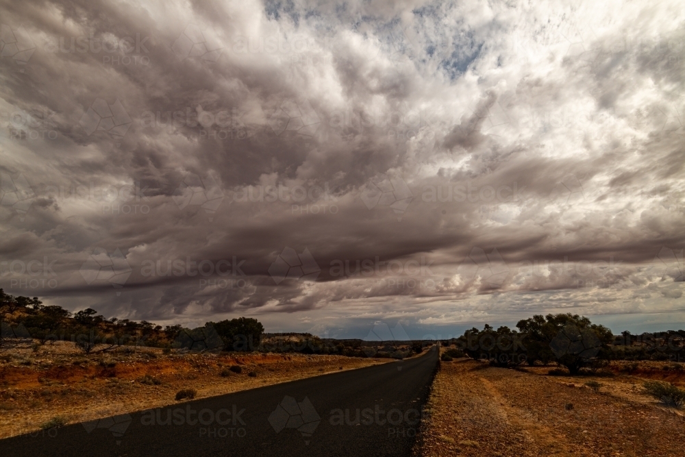 View of long straight bitumen road to horizon with dramatic stormy clouds - Australian Stock Image