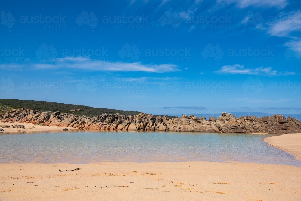 View of shallow pool on beach with rocks in the background with house on the hill - Australian Stock Image