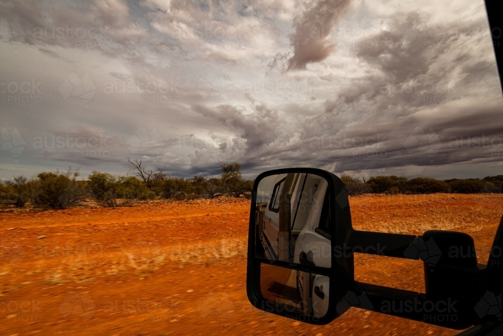 View out a car window of desert country with dramatic stormy sky and mirror view of vehicle. - Australian Stock Image