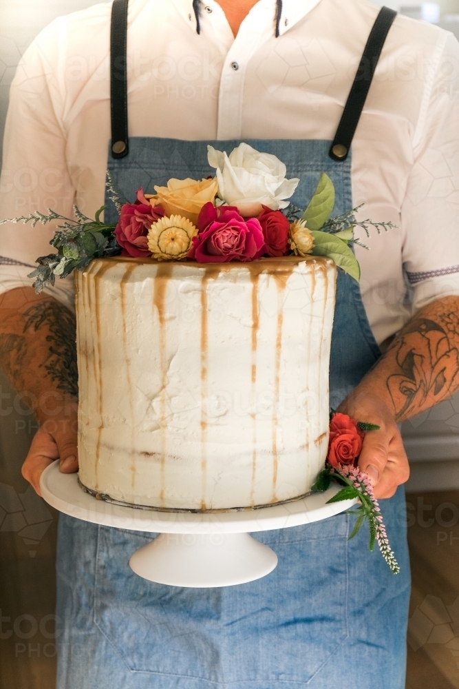 Waiter carries tall wedding cake with flower topper - Australian Stock Image