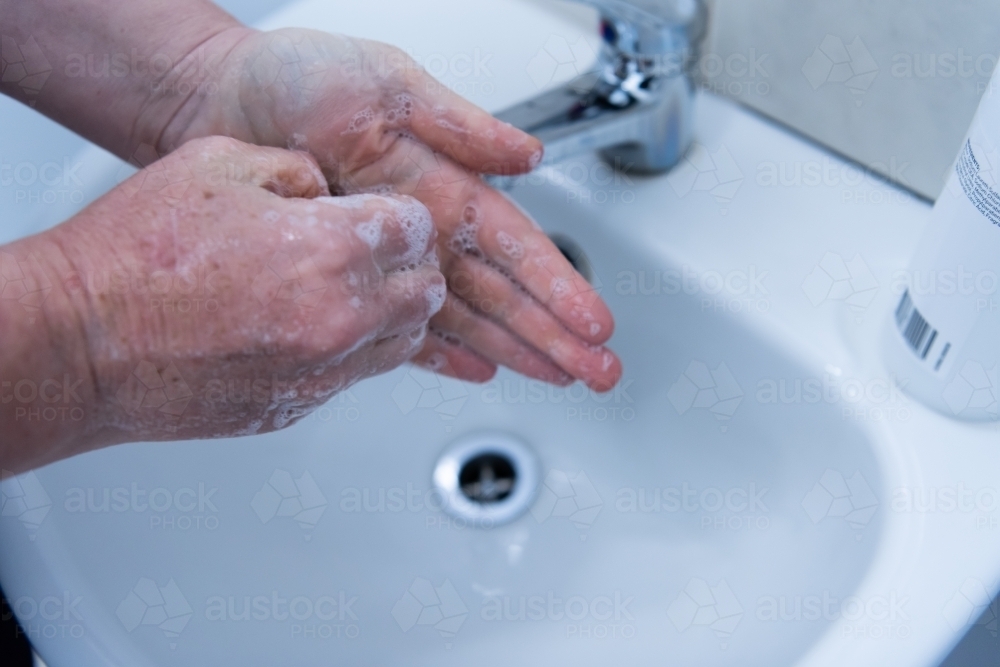 Washing hands with soap and water at basin - Australian Stock Image