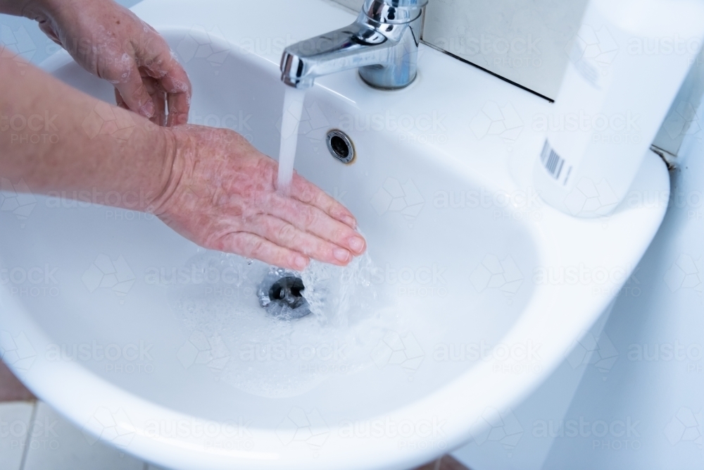 Washing hands with soap and water at basin - Australian Stock Image