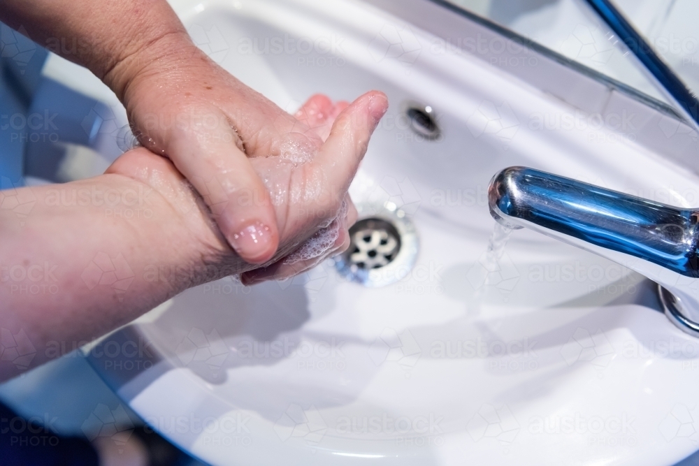 Washing hands with soap and water at basin - Australian Stock Image