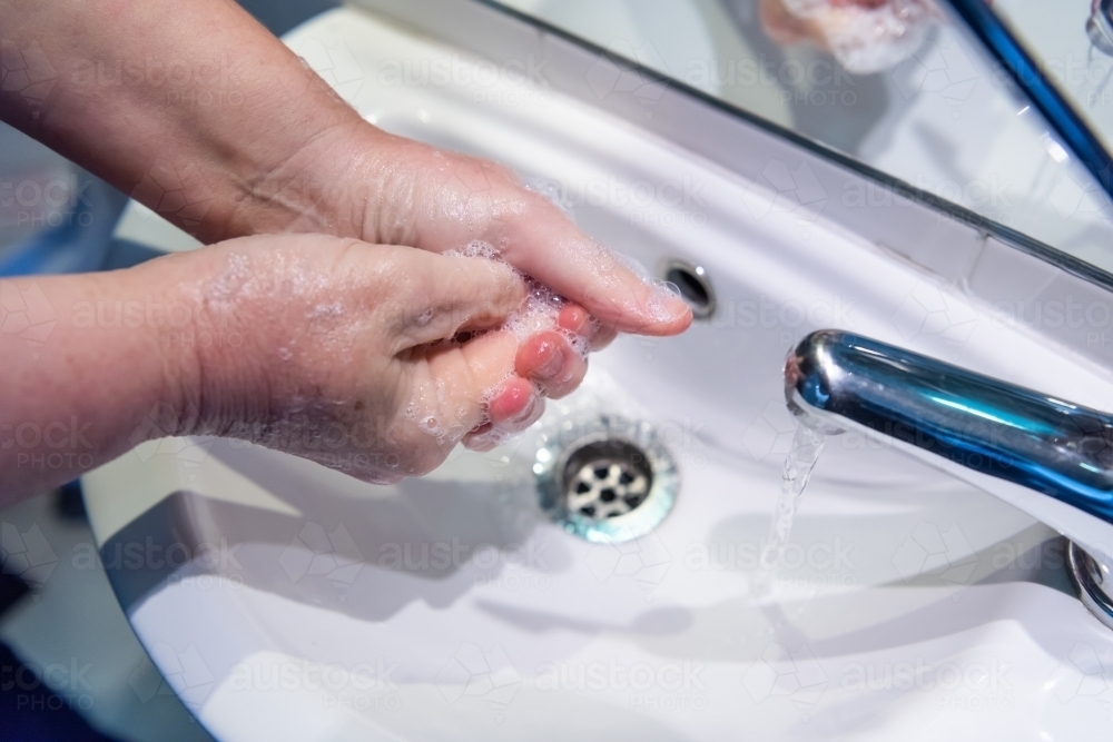 Washing hands with soap and water at basin - Australian Stock Image