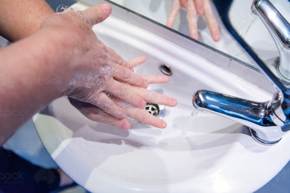 Washing hands with soap and water at basin - Australian Stock Image