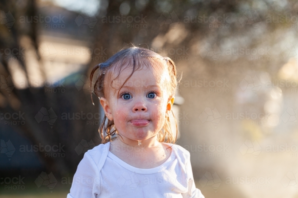 Water dripping off face of little kid after playing under sprinkler in yard of home - Australian Stock Image