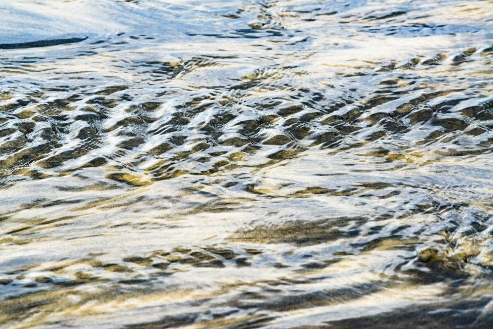 Water rippling over yellow and black mineral sands on a beach - Australian Stock Image