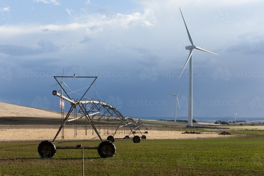 Water sprayer in paddock with wind turbines in background - Australian Stock Image