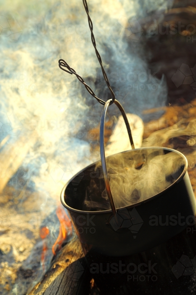 Water steaming in the black billy billycan over a campfire - Australian Stock Image