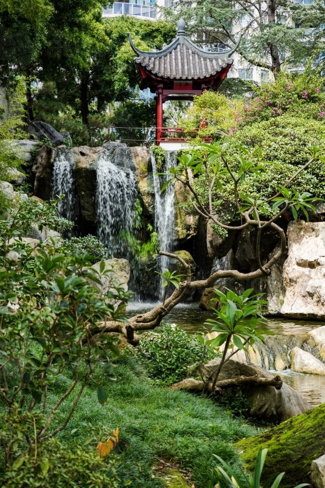 waterfall and small pavilion with city buildings in background - Australian Stock Image