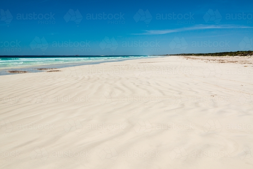 wave patterns on a white sand beach leading to a far horizon and dark blue sky - Australian Stock Image