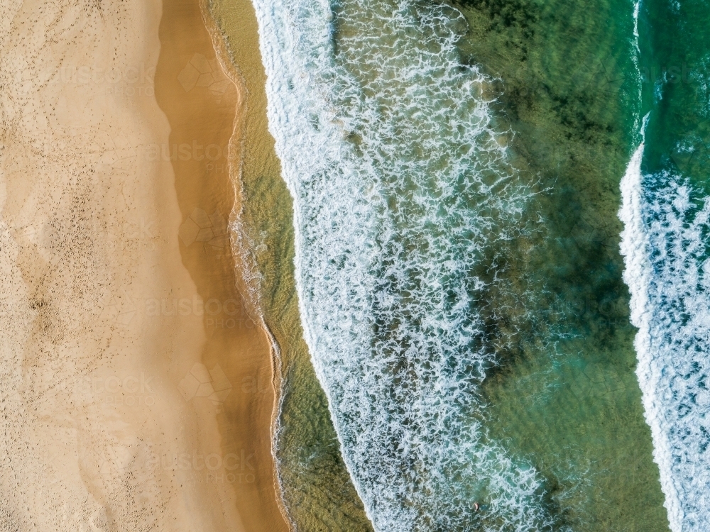 Waves washing up to empty beach full of footprints - water and sand seen from above - Australian Stock Image