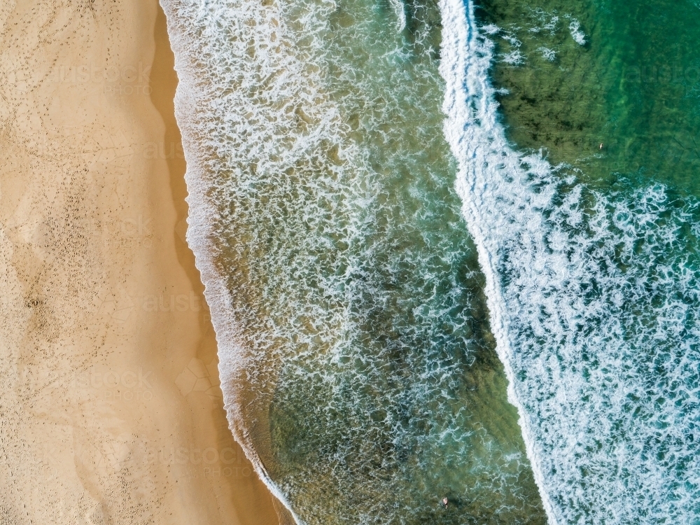 Waves washing up to empty beach full of footprints - water and sand seen from above - Australian Stock Image