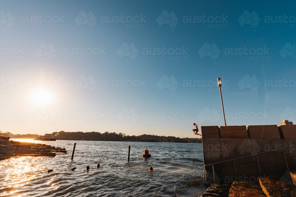 Wet kids jumping from ledge into water at Marrinawi Cove in bright afternoon sunshine - Australian Stock Image