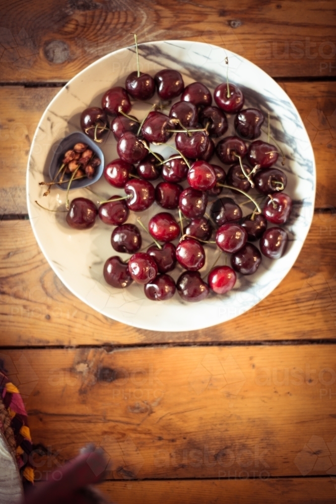 White bowl of cherries and pips on wood table - Australian Stock Image