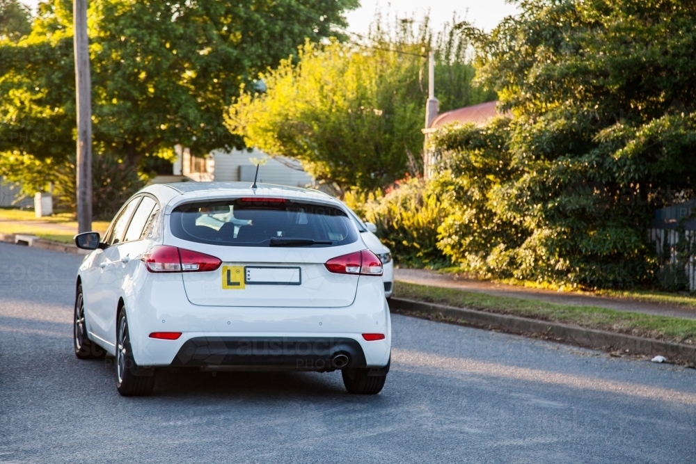 White car with l plate driving on quiet suburban road - Australian Stock Image