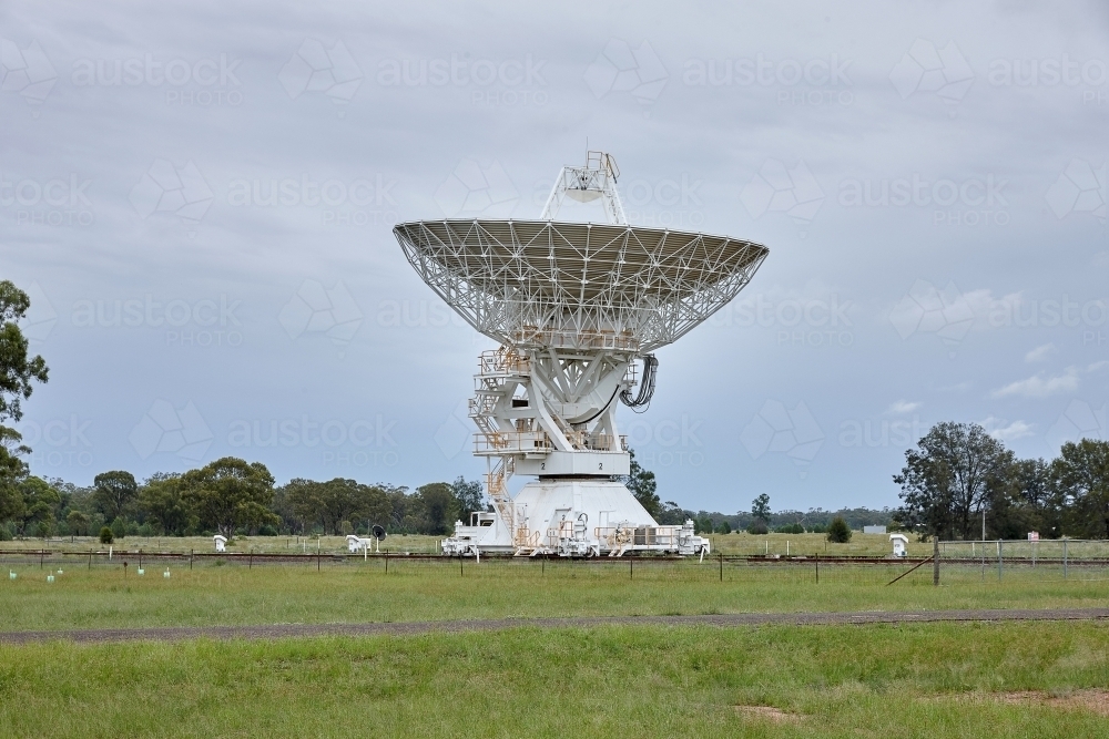 white radio telescope in a field on a cloudy day with trees on the side - Australian Stock Image