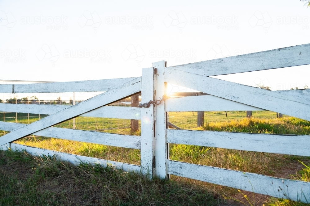 White wooden post and rail fence and gate backlit with sun flare - Australian Stock Image