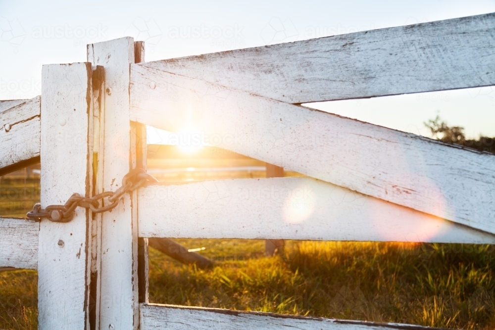 White wooden post and rail fence and gate backlit with sun flare - Australian Stock Image