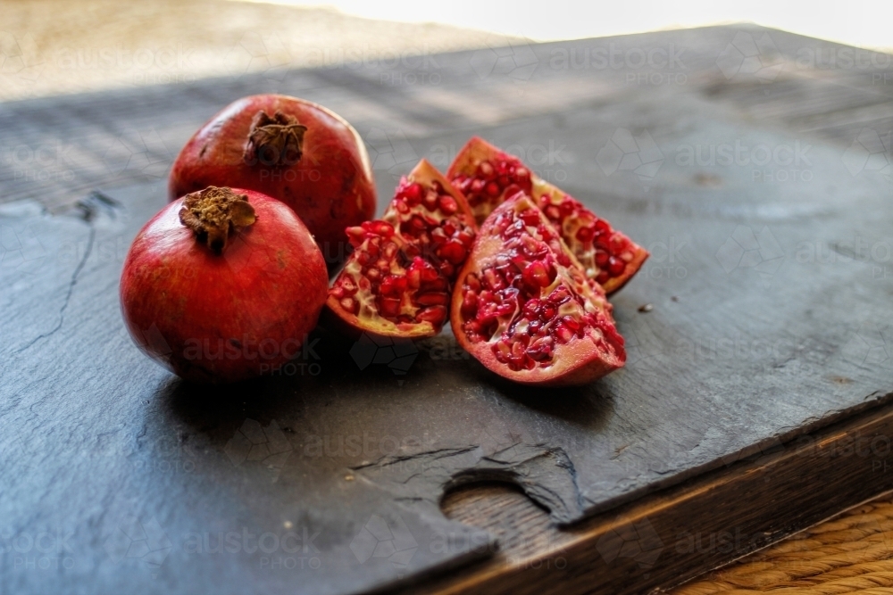 Whole and cut pomegranates on black slate - Australian Stock Image