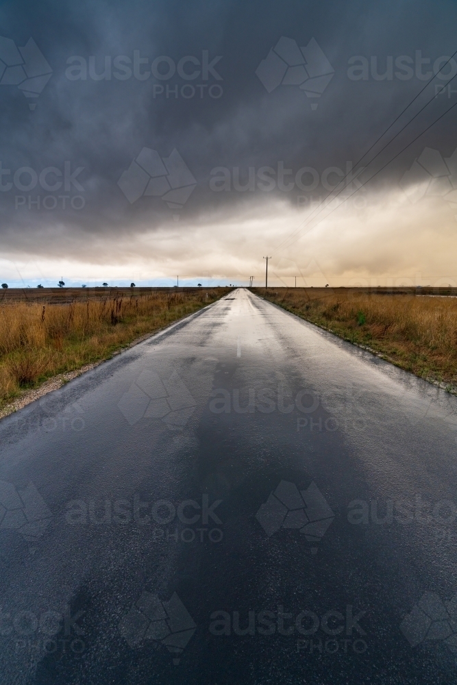 Wide angled view down a country road with bright gap under dark storm clouds - Australian Stock Image