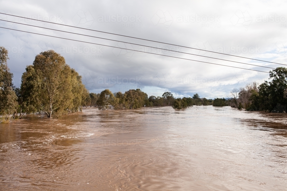 wide brown river full of floodwater during natural disaster flood - Australian Stock Image