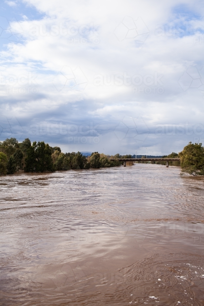 wide brown river full of floodwater during natural disaster flood - Australian Stock Image