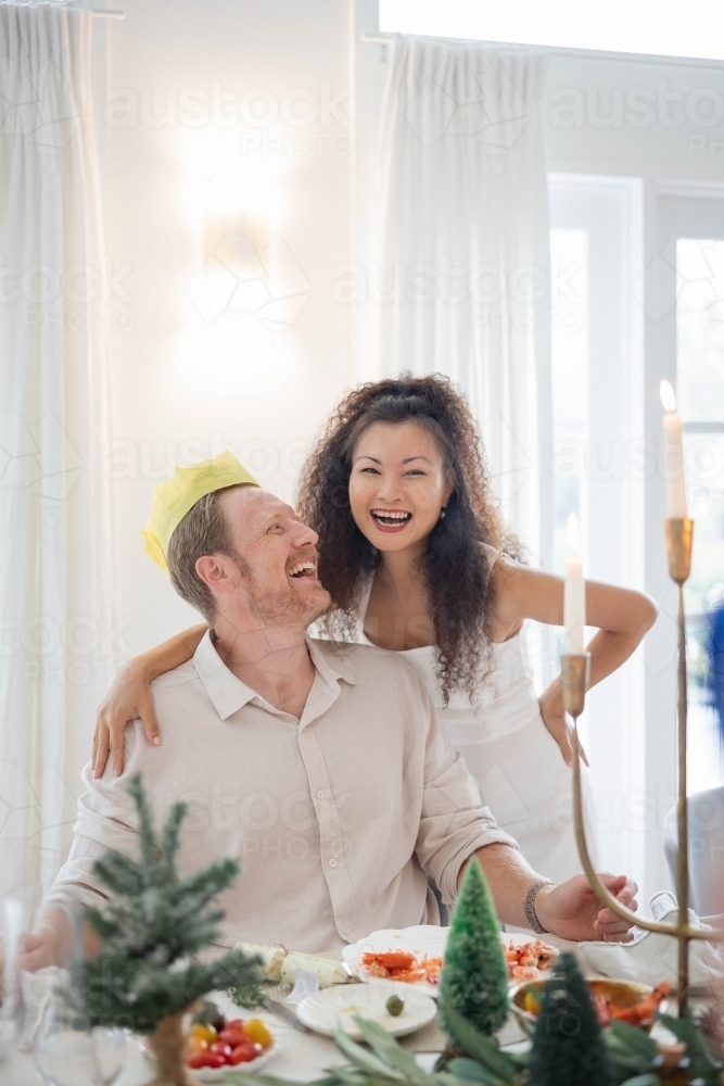 Wife and husband wearing Christmas crown at dining table - Australian Stock Image