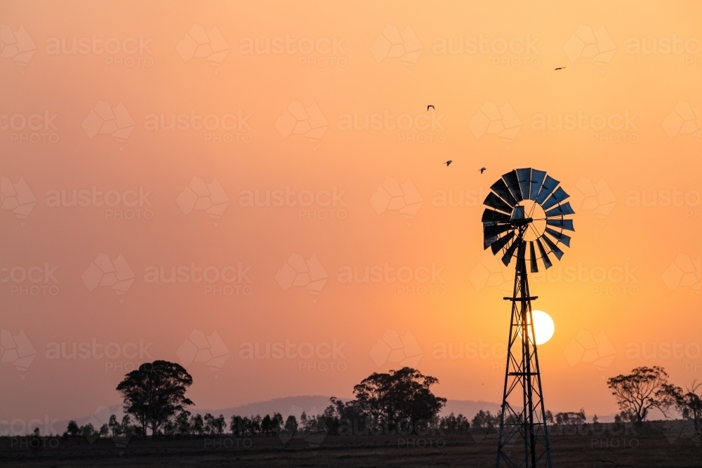 Windmill against a smoky sunset in drought conditions - Australian Stock Image