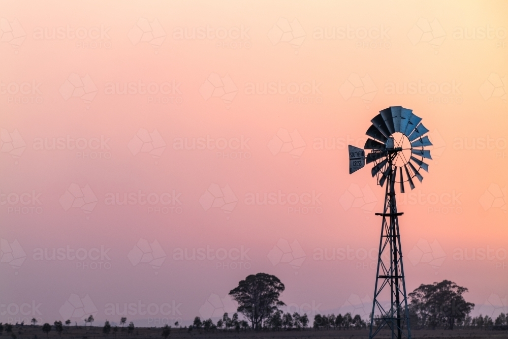 Windmill against a smoky sunset in drought conditions - Australian Stock Image