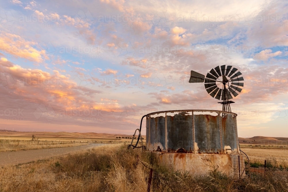 windmill and old rusty water tank at sunset - Australian Stock Image