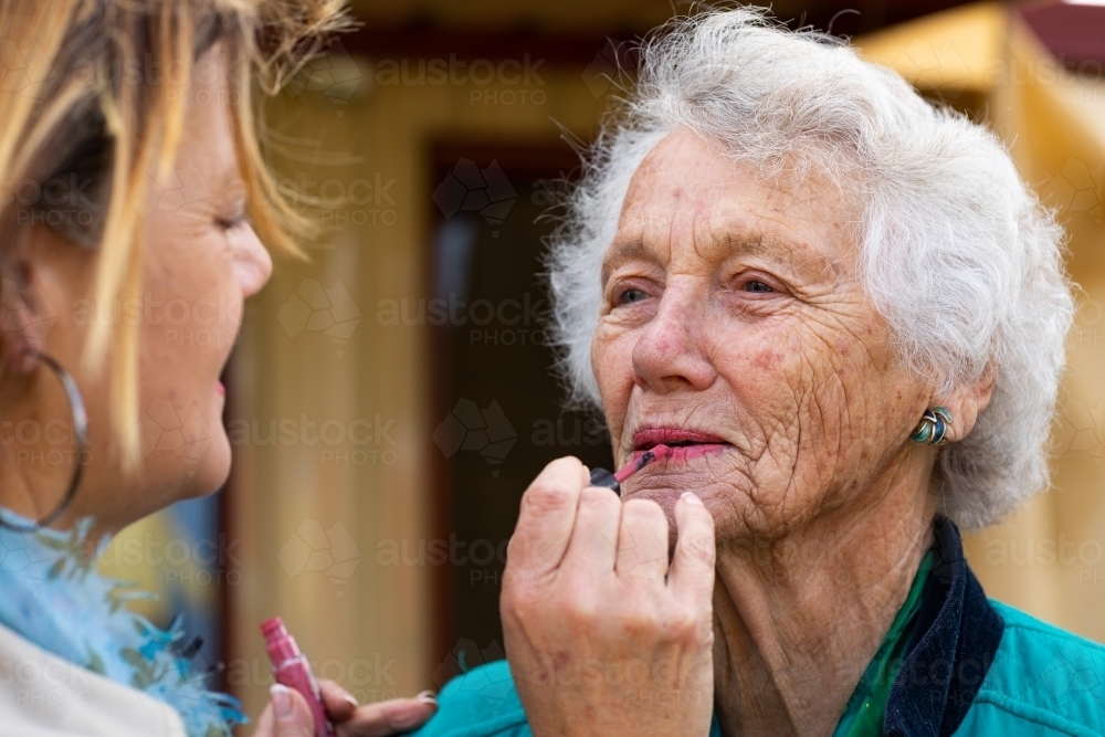 woman applying lipstick to her elderly mother's lips - Australian Stock Image