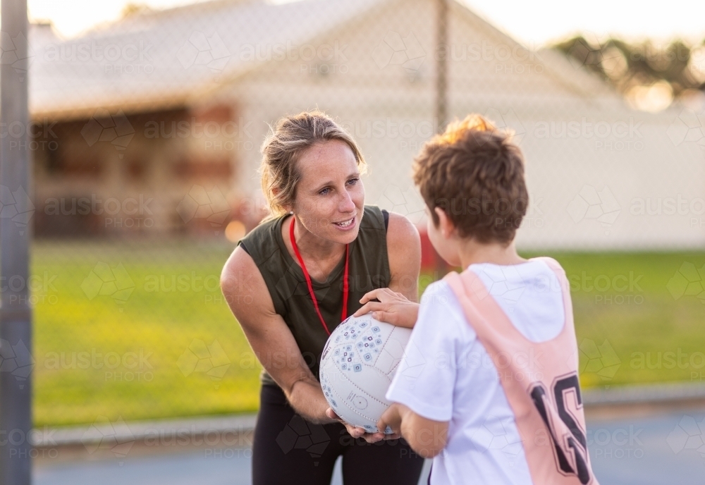 woman coaching child holding netball on court - Australian Stock Image