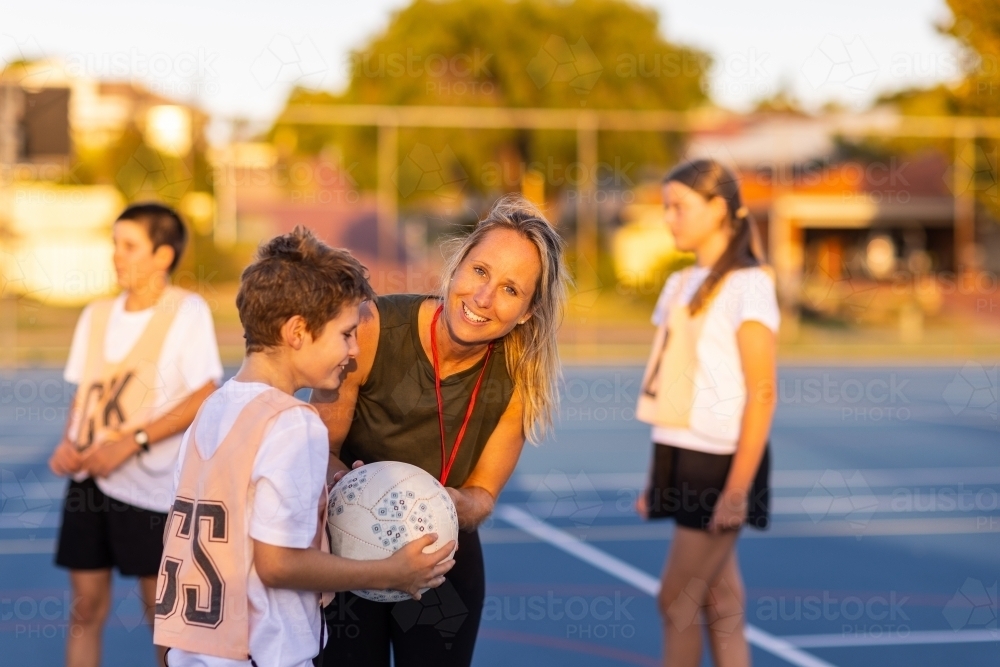 woman coaching children in netball team, leaning over child and looking at camera - Australian Stock Image