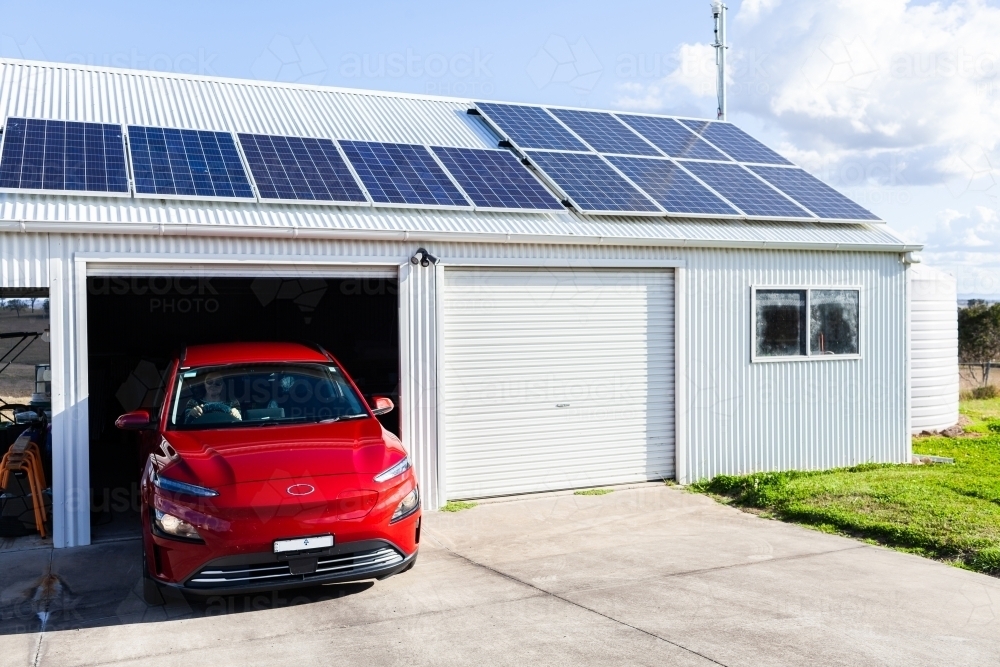 Woman driving electric car out of solar powered shed on country farm  - living sustainably - Australian Stock Image