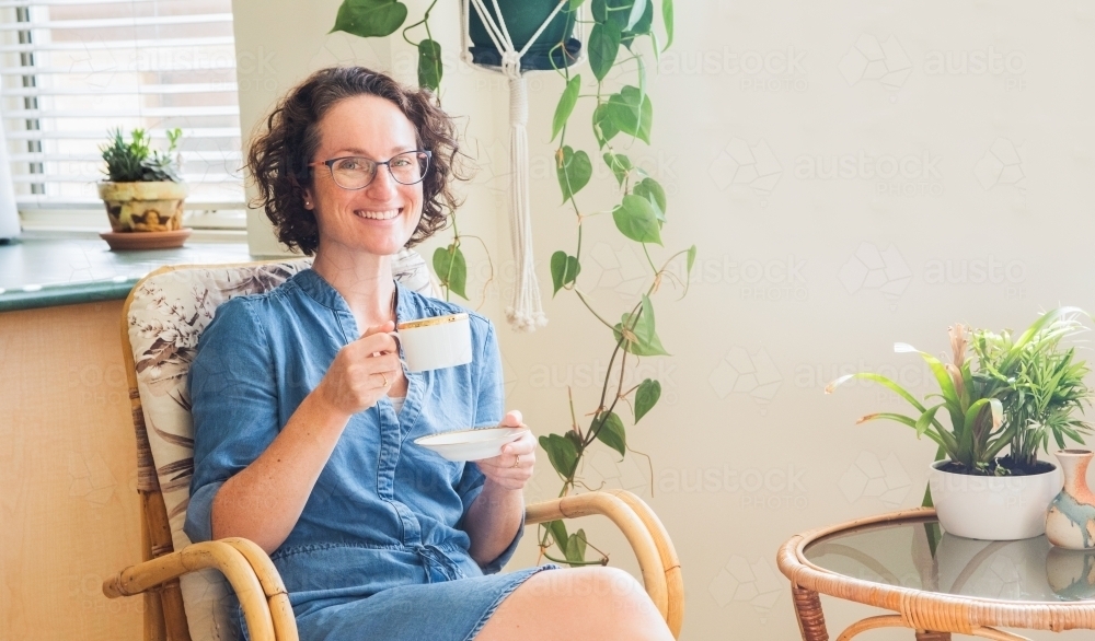 Woman having a cup of tea smiling at the camera in her home - Australian Stock Image