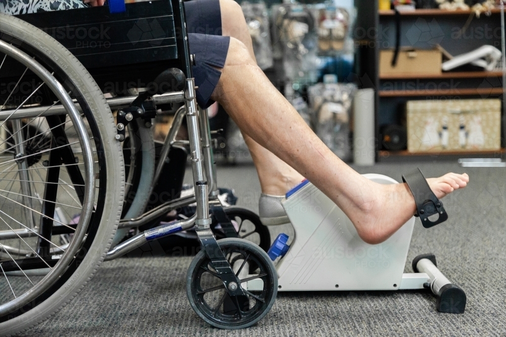 Woman in wheelchair doing stretches using pedaling machine - Australian Stock Image