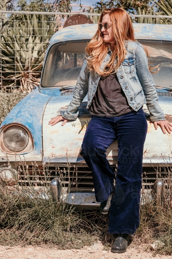 Woman leans against old car. - Australian Stock Image