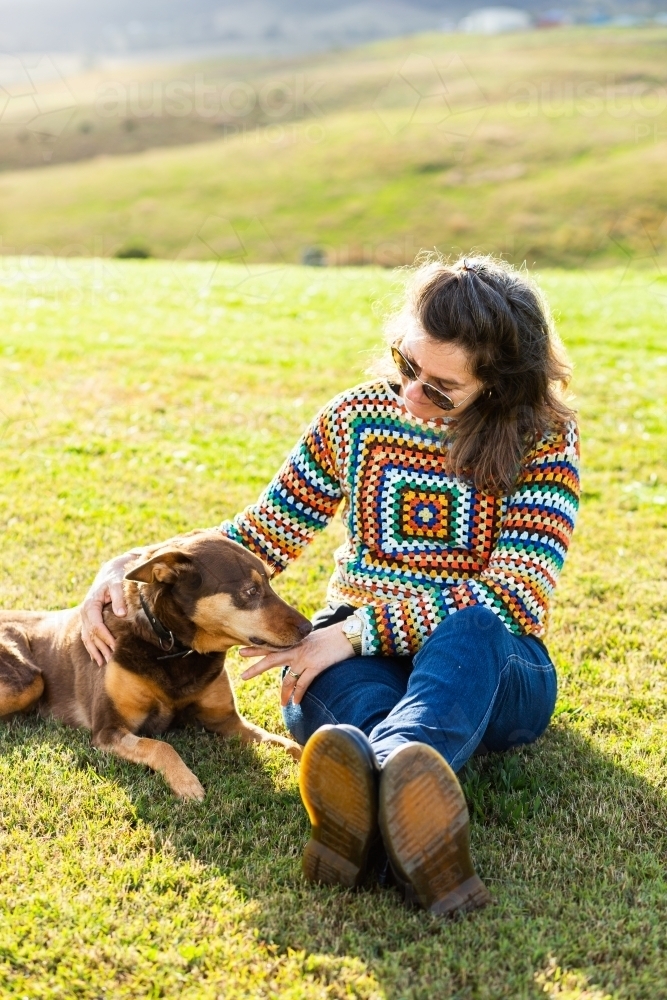 woman looking down at old pet kelpie dog resting on lawn on farm - Australian Stock Image