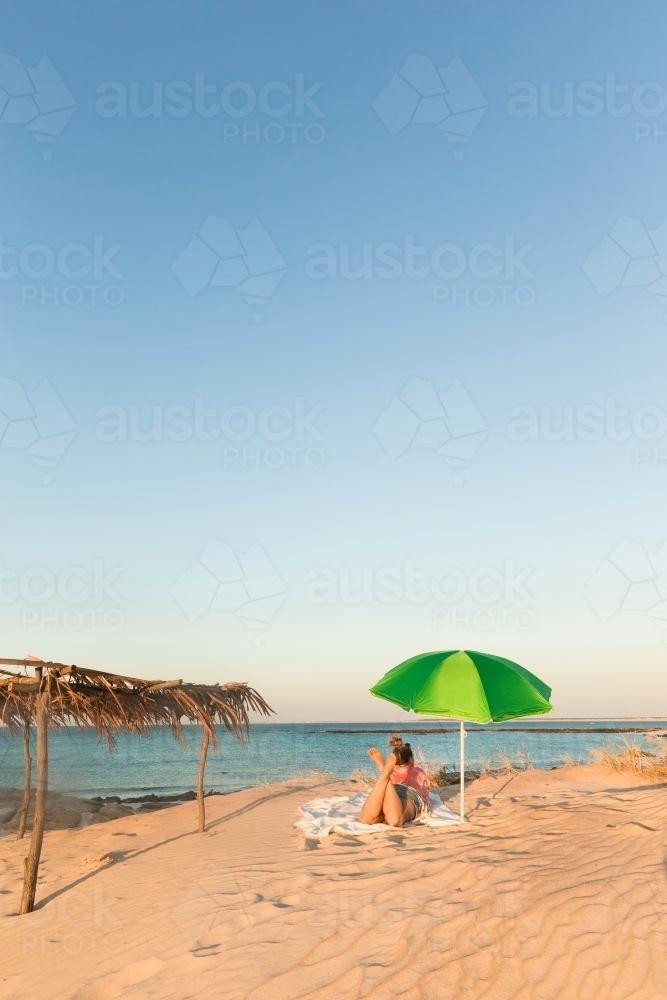 Woman lying under a beach umbrella on the sands of cape leveque - Australian Stock Image