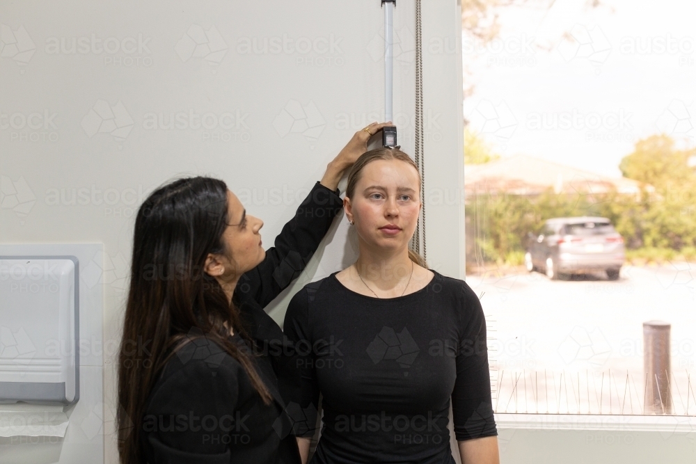 woman measuring the height of another woman using a height ruler on the wall of medical practice - Australian Stock Image