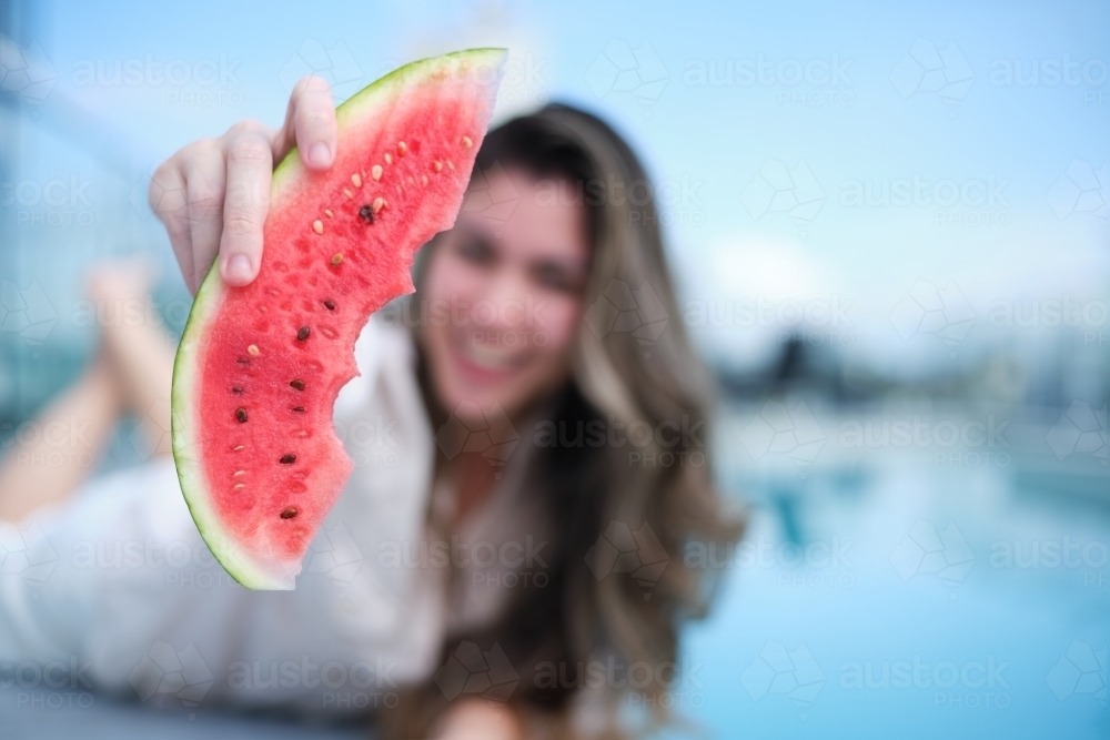 Woman out of focus holding watermelon slice up to camera - Australian Stock Image