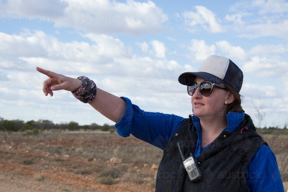 Woman outdoors with 2-way radio, pointing into distance - Australian Stock Image