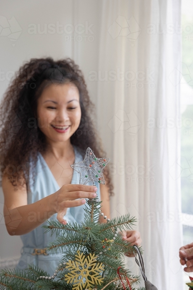 Woman placing star on Christmas tree - Australian Stock Image