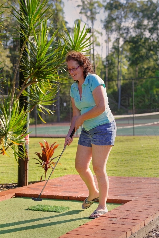 Woman playing mini golf or putt-putt in the late afternoon sun - Australian Stock Image