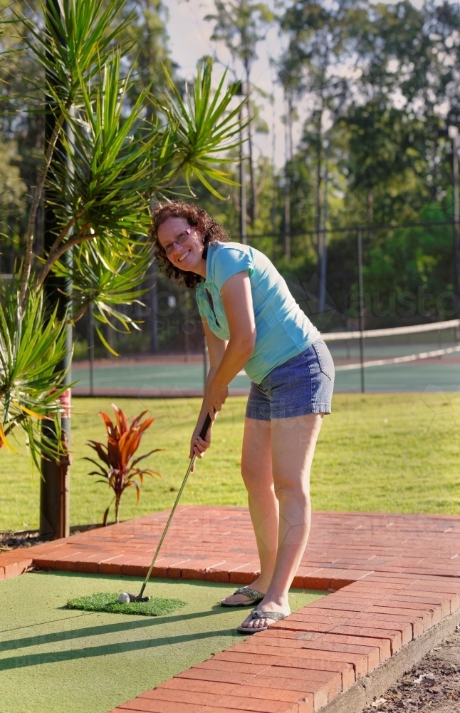 Woman playing mini golf or putt-putt in the late afternoon sun - Australian Stock Image