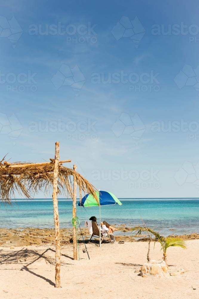 Woman relaxing under beach umbrella on the coast - Australian Stock Image