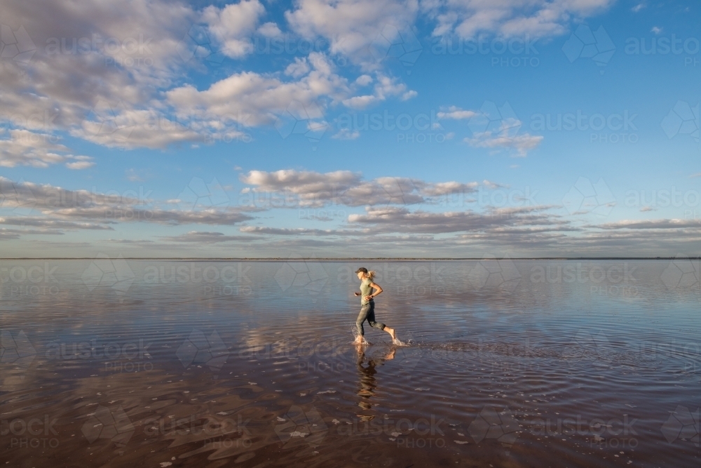 Woman running along on the top of a salt lake. - Australian Stock Image